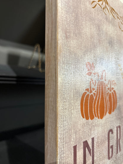 Close-up side view of a rustic wooden sign with a distressed background, and orange pumpkins.