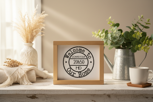 Decorative sign with 'Welcome to Leonardtown 20650 MD' on a shelf with plants and a mug.