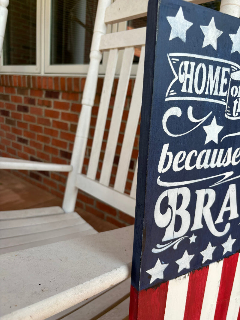 Decorative sign with American flag design and text on a porch.