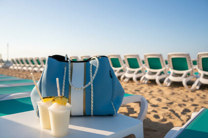 Blue bag with white straps on a chair next to a drink with a straw and pineapple slice.
