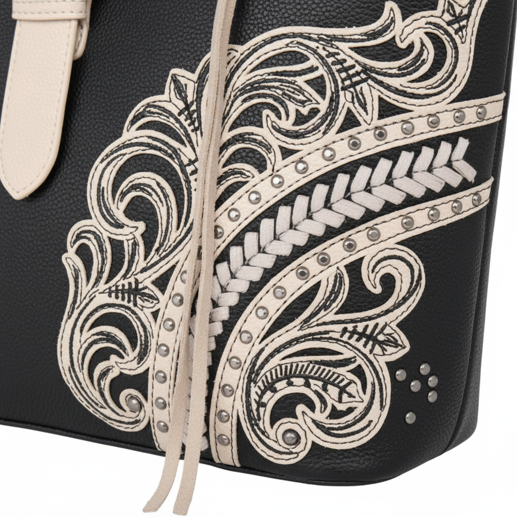 Close-up of a black textured leather bag featuring intricate western-style embroidery in cream with silver-tone studs and a matching cream drawstring.