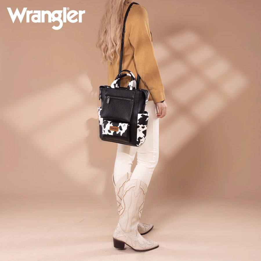 Person holding a black and white cow print bag with 'Wrangler' branding on a beige background