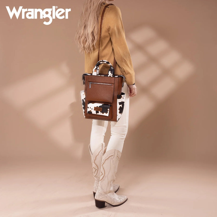 Person wearing a brown leather backpack with cow print design, standing against a beige background with 'Wrangler' branding.