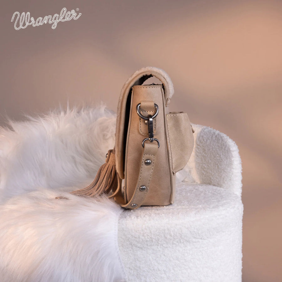 Beige handbag with tassel on a white furry surface, Wrangler logo visible