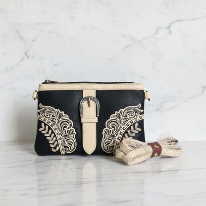 A black and khaki Montana West clutch/crossbody bag with floral embroidery, a belt buckle, and a detachable strap.