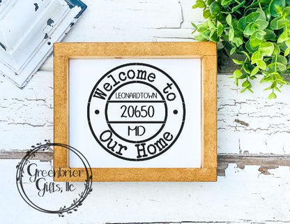 A personalized wooden sign with 'Welcome to Our Home' text with the text '20565'. The sign is placed in a rustic wooden frame.
