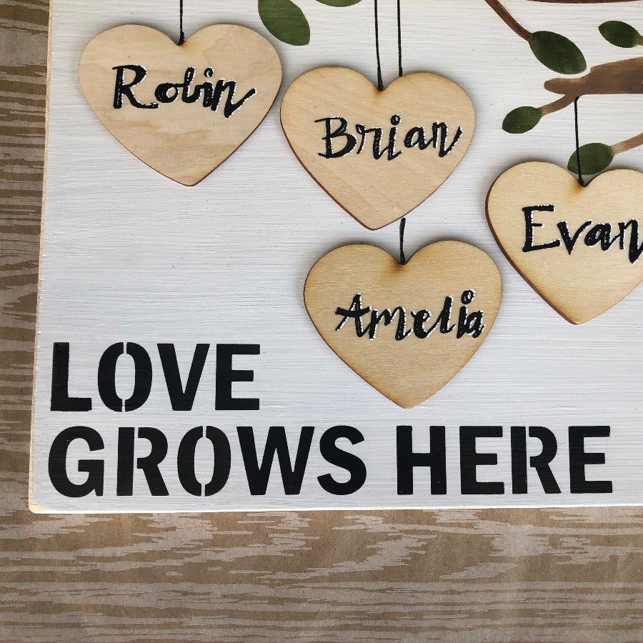 close up of love grows here sign corner showing wood hearts hanging from tree limbs