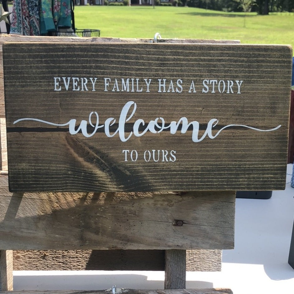 Every Family has a story welcome to ours sentiment painted onto a wood hangable sign stained espresso