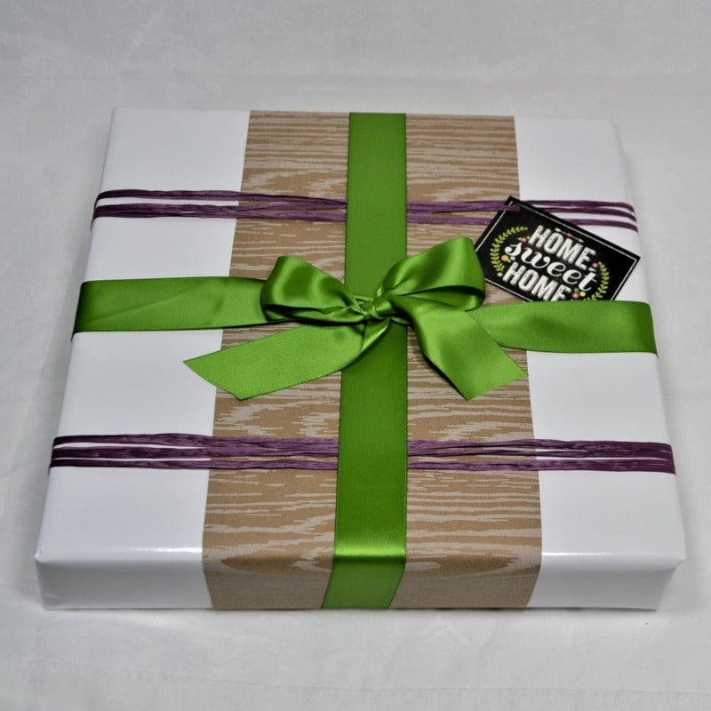 medium gift box wrapped with thick glossy white paper and tied with purple raffia and green ribbon