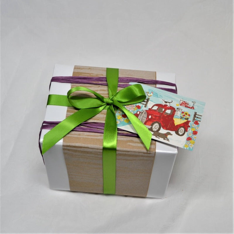 Small gift box wrapped with thick glossy white paper and tied with purple raffia and green ribbon