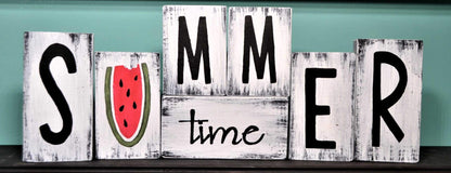 white distressed wood blocks that sit on a shelf. Hand painted SUMMER time in black letting with watermelon missing a bite as the U on distressed white block.